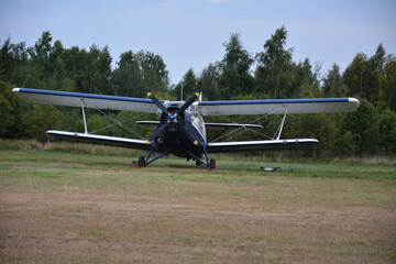 aircraft, A vintage biplane with blue and white coloring sits on a grassy field, surrounded by trees © Mariia