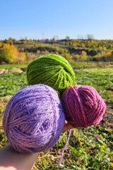 Three colorful knitting yarns with a serene autumn scene on the background. The essence of cozy knitting in the fall, the warmth and comfort of handmade crafts 