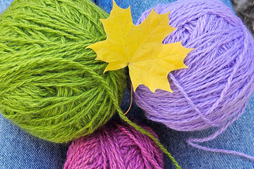 Autumn Knitting Essentials: colorful threads, needles, and a cozy project in progress, complemented by a yellow maple leaf. Warm and relaxed knitting outdoors.