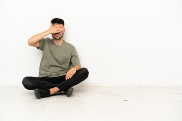 Young caucasian man sitting on the floor isolated on white background covering eyes by hands. Do...