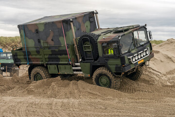 army truck drives diagonally over a sand mountain on the beach