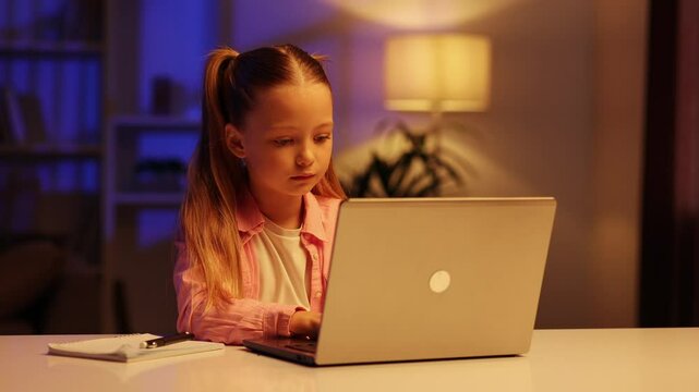Online development of children. Little blond girl using online education platform, working on laptop, sitting at home, clicking on keyboard, slow motion.