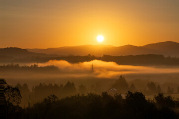 Sunrise over misty hills with mountains in the background