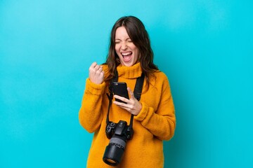 Young photographer woman isolated on blue background with phone in victory position