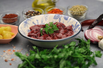 Cut raw beef liver with onions, spices, chili peppers and dill on wooden table, flat lay