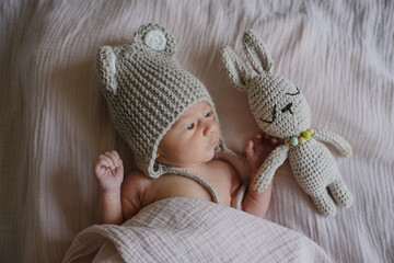 A newborn baby in a knitted hat on a blanket with a small bunny, a soft toy. Just born