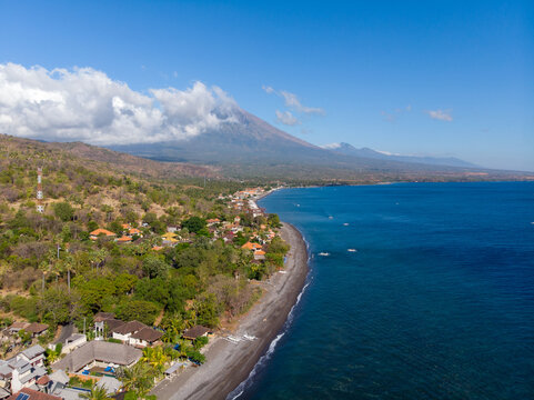A breathtaking coastal view meets a towering mountain under clear blue skies.