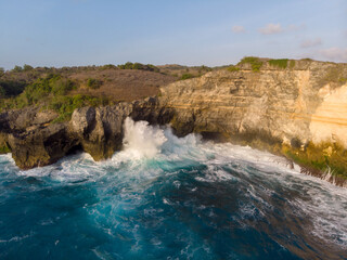 Naklejka premium Waves crashing against the rocky cliffs under a clear sky.