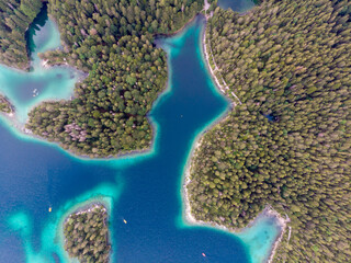 Aerial view of a serene lake surrounded by lush forests with vibrant blue and green waters.