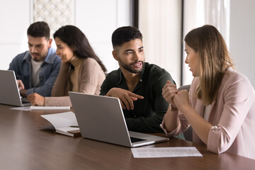 Serious young Arabic mentor training intern at laptop, speaking to coworker woman, explaining work task. Two multiethnic business colleagues talking at table, discussing corporate communication
