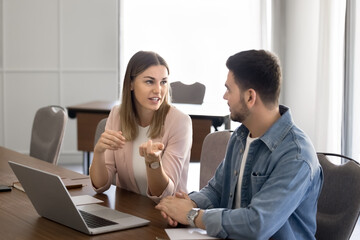 Two company employees working on project at laptop together, meeting at workplace table for teamwork, talking at computer, discussing business plan, communication