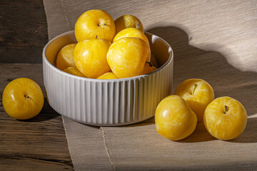 ripe sweet yellow plums in a ceramic bowl on a wooden table