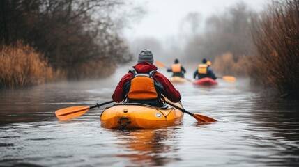 Rear view of kayakers paddling down a river in a foggy morning.
