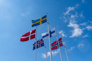 Scandinavian countries flags waving on metal poles against blue sky.