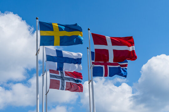 Scandinavian countries flags waving on metal poles against blue sky.