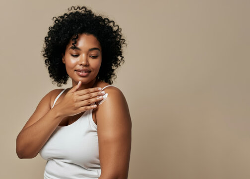 A biracial young woman plus size model girl applies cream on beige background