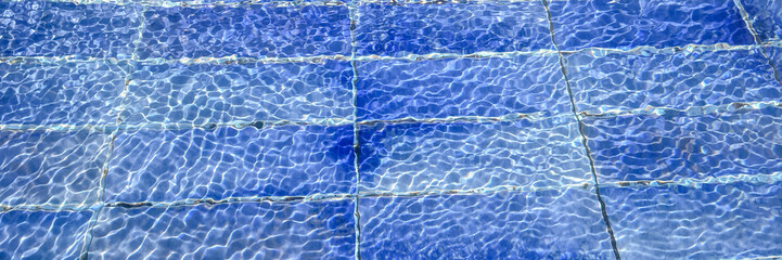 Clear blue water ripples over pool tiles on a sunny day, evoking relaxation and summer vacation vibes