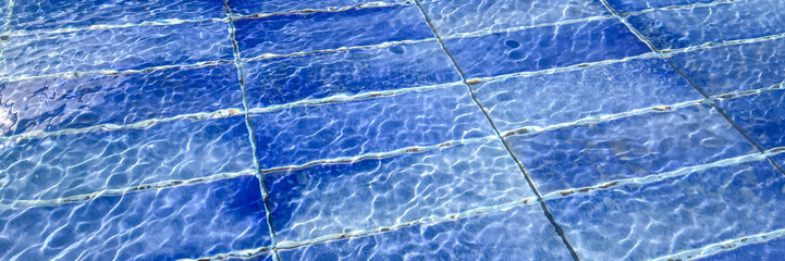 Close-up of rippling water over blue tiles in a swimming pool, evoking summer relaxation and...