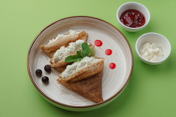 Thin crepes with sour cream, chocolate, and berries on a plate, top view