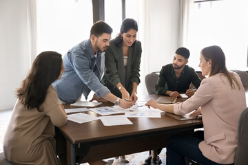 Focused busy diverse project colleagues analyzing sales statistic charts, discussing paper reports,...