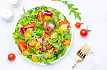 Vegan vegetable salad with red and yellow tomatoes, cucumber, red onion, green lettuce and arugula. White background, top view