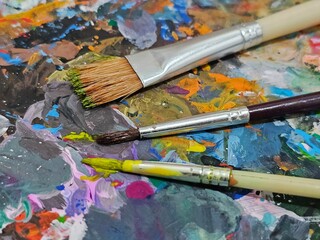 Fototapeta premium Tangerang, Indonesia - October 12, 2024: Paint brush for painting. With colorful oil artist paint palette board background. Oil paint brush.