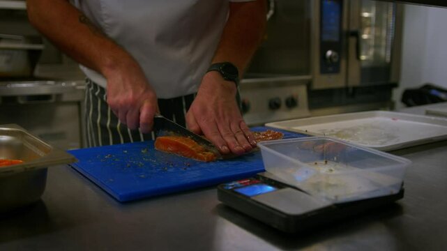Professional chef cuts up fish as he prepares food in a professional kitchen