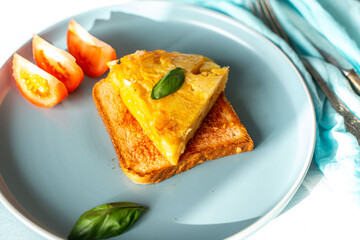 Spanish omelette or tortilla de patata with potatoes and onions on toast with tomatoes and basil on a blue plate. Typical Spanish cuisine.