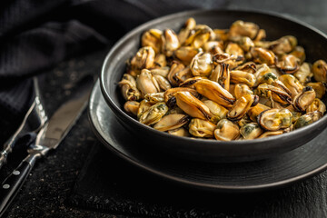 Shelled mussels meat on plate on black table.