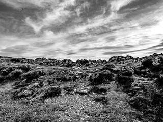 A winding rocky path traverses the rugged terrain, surrounded by boulders and dry grass, beneath a dramatic sky filled with clouds during late afternoon light.