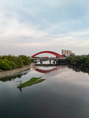 Traffic bridge over river in Ho Chi Minh City, Vietnam from aerial view featuring two large red steel arches and a wide, ten lane highway for heavy vehicles. Low angle with reflection and bouy