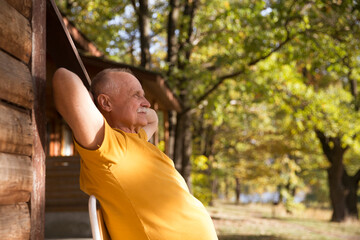 smiles elderly man sits next to his log house and enjoys a warm autumn day. cottage core.