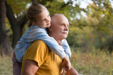 smiling child girl hugs grandpa On Walk in the autumn outdoors. Concept of friendly family. copy space. banner
