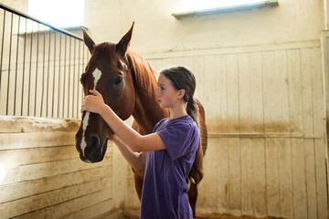 Teen girl with brown horse in the stables