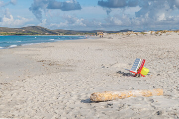 Two empty chairs, one white and one red, on the wide sandy beach of Is Arenas Biancas, Sardinia, Italy
