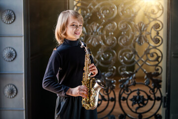 A young boy is playing a saxophone in front of a wrought iron gate.