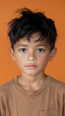 Close up Portrait of a asian boy wearing a brown shirt against an orange background