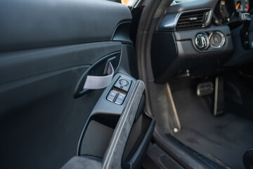 Interior view of a car door panel with window controls, fabric pull handle, and stitched armrest...