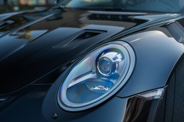 Fototapeta premium Close-up of a sleek car's LED headlight with colorful reflections on a glossy black hood.