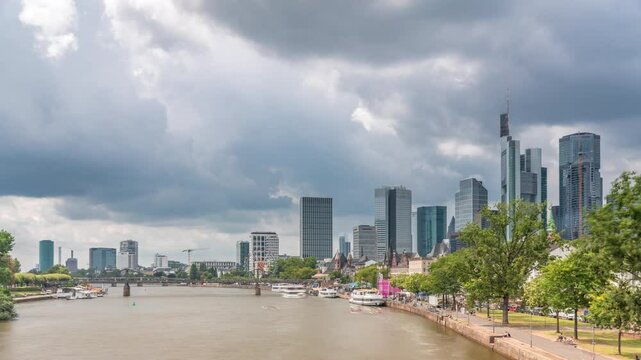 Hyperlapse of the historical Eiserner Steg (Iron Bridge) over the Main River in Frankfurt, Germany. Skyscrapers skyline and waterfront reflect in the water under a cloud-filled sky timelapse