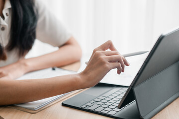 Close-up of a person using a stylus on a tablet with a keyboard, working at a desk in a bright...