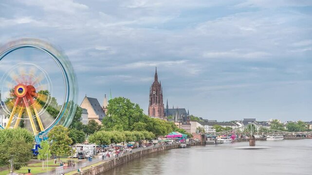 Aerial hyperlapse of pleasure boats on the Rhine Main, framed by the spire of Kaiserdom St. Bartholomaus. Eiserner Steg bridge and Ferris wheel add vibrancy to Frankfurt's scenic waterfront timelapse