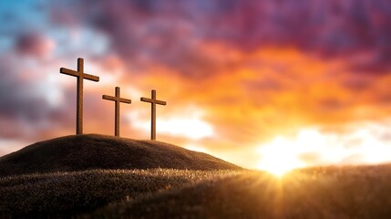 Silhouetted crosses standing tall on a rolling hill set against a vibrant sunset sky with dramatic clouds glowing in shades of orange and purple