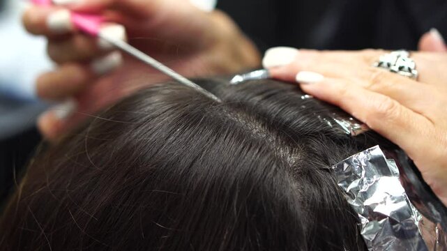 Beauty salon. Professional stylist combs client hair after applying paint with brush. hair coloring in hairdressing salon. Close-up of hairdresser in beauty salon. Painting on foil