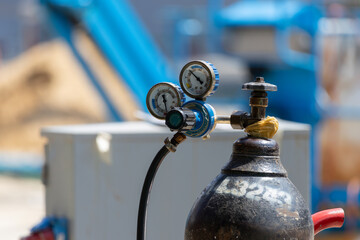A blue and white pressure gauge sits on top of an oxygen cylinder tank with site construction...