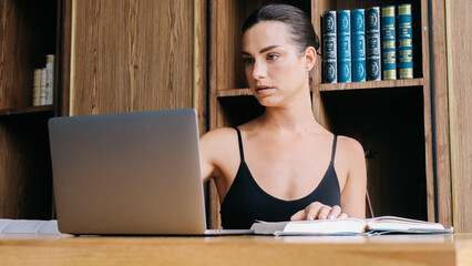 A young woman in a modern office or library studies material on her laptop, deepening her knowledge and skills. The atmosphere promotes skill enhancement and professional growth.