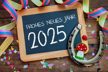 Wooden hang tag and slate with four leaf clover and sparklers with the german words for happy new year - frohes neues jahr 2025 on wooden weathered background