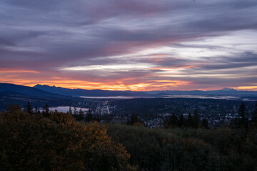Obraz premium Sunrise over Fraser Valley at Port moody, BC, as viewed from a residence at UniverCiity Highlands on Burnaby Mountain, BC, with mountains in silhouette on horizon.