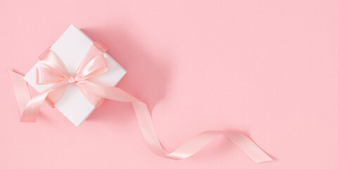 Holiday pink background. Gift box and satin ribbon on soft pink background. Flat lay, top view, copy space, banner