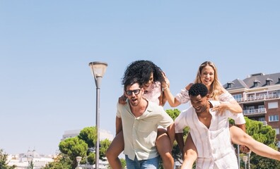 Cheerful diverse friends enjoying piggyback ride in park